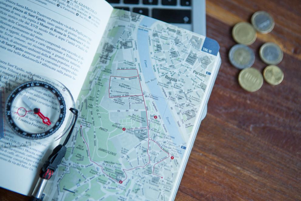 Holiday planning with a computer, a map, a compass and coins
